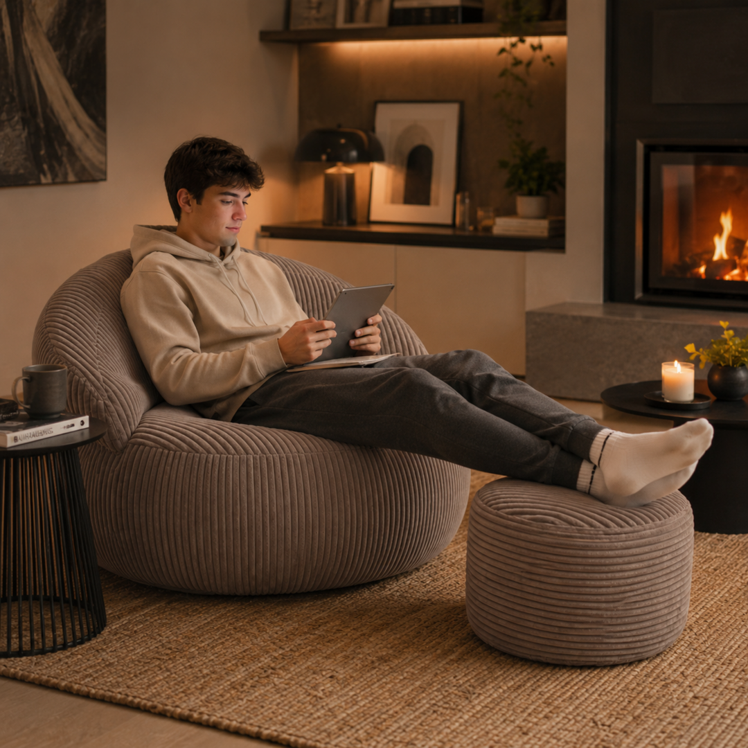 Personne assise confortablement sur un pouf XXL en velours côtelé avec repose-pieds, dans un salon