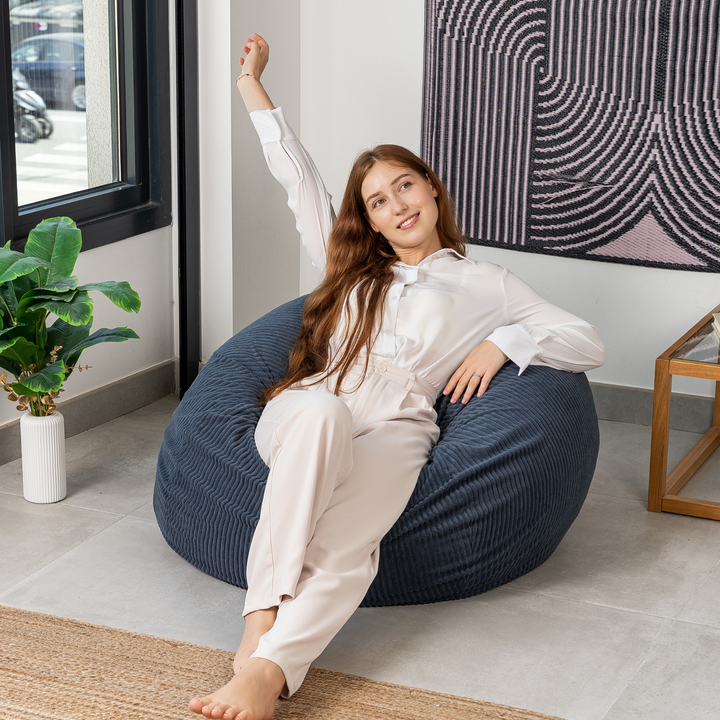 Femme assise sur un pouf poire déhoussable en velours côtelé, dans un salon