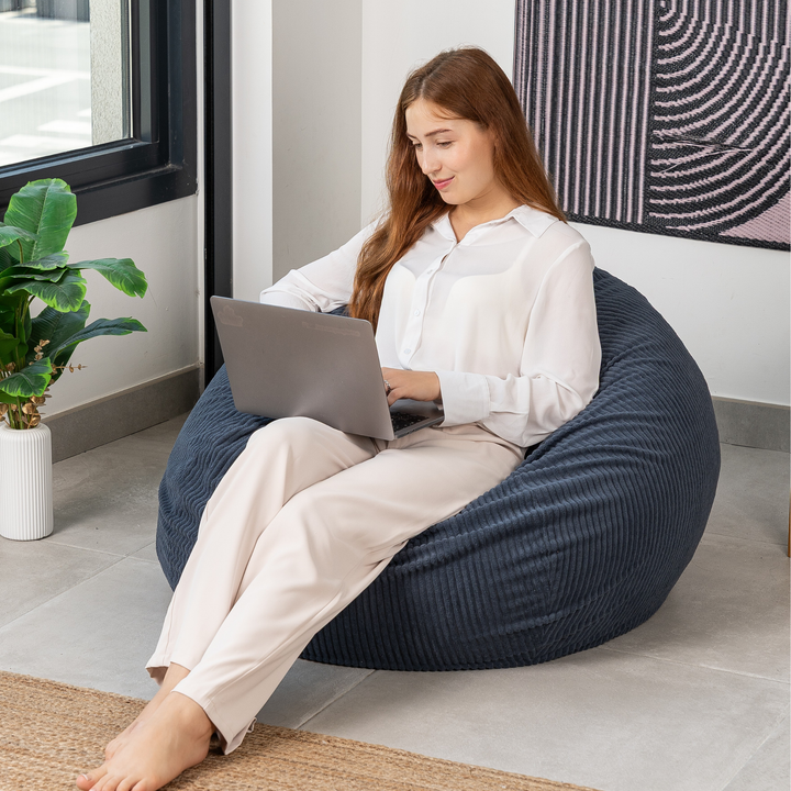 Femme assise sur un pouf poire déhoussable en velours côtelé, dans un salon