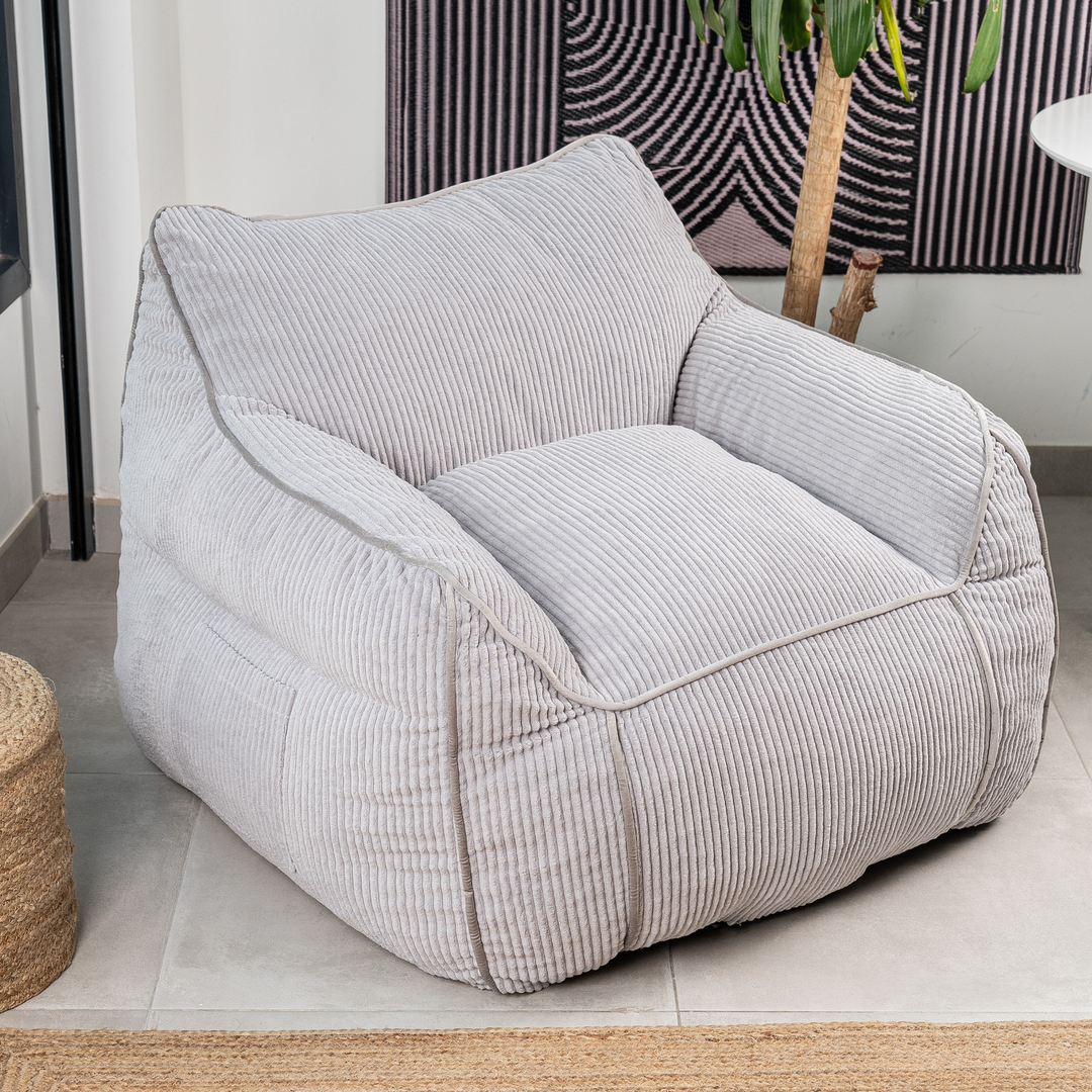 Pouf fauteuil velours côtelé gris clair, accoudoirs intégrés, dans un salon